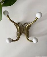 Front view of brass butterfly coat hook with four white ceramic tipped hooks on a white background.
