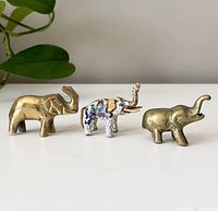 Front view of three small elephant figurines including two brass and one cloisonné with enamel and gold accents