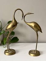 Pair of vintage brass flamingo figures displayed side by side showing full figure details and brass tone.
