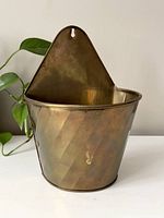 Front view showing the diagonal ridged brass wall pocket with hanging tab and patina