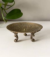 Front view showing embossed floral design on top flat plate and three decorative curled legs.