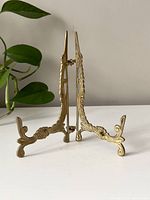 Side view of vintage brass picture frame stand showing ornate curved feet and detailing