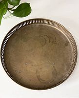 Top-down photo of round brass serving tray showing patina and wear marks, with a houseplant in the background.