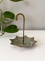 Front view of vintage brass umbrella-shaped dish showing the umbrella sections and curved central handle with green patina and wear marks.