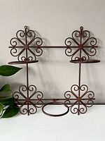 Front view of vintage metal hanging garden planter with three circular holders and decorative scroll design.