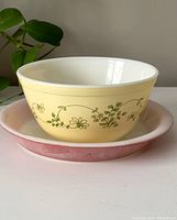 Photo showing the yellow Pyrex mixing bowl with green floral pattern held over the pink pie plate on a flat surface