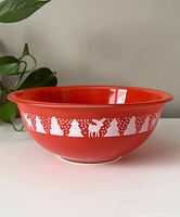 Side view of red Pyrex mixing bowl decorated with white Christmas shapes including trees, snowmen, and reindeer.