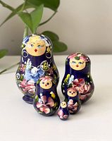 Front view of the 5 nesting dolls arranged together showing floral painted designs on dark blue background.