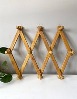 Front view of vintage wooden accordion peg rack extended showing the light wood and peg details.