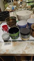 Overview of assorted small pots and containers including ceramic, metal, and glass jars, placed on a table.