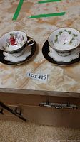 Two bone china cups and saucers placed on a beige countertop with floral designs inside the cups, black outer surfaces, and gold trim.