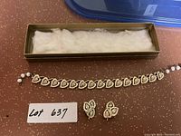 Full view of bracelet and matching clip-on earrings inside a box with white padding, showing jewelry lot and lot number tag.