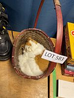 Orange and white cat figurine curled up sleeping inside a woven basket with handle.