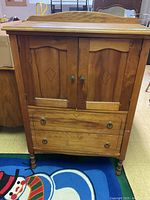 Front view of wooden dresser showing two paneled doors with decorative inlay and two drawers with metal ring pulls.