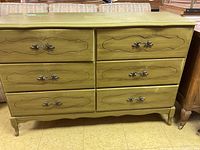 Front view of a green wooden dresser with six drawers and decorative carved designs on drawer fronts.
