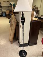 Full view of black metal floor lamp with white fabric shade against a basement background