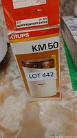 Photo of the Krups KM 50 Coffee Grinder packaging with label Lot 442 showing the coffee grinder with white base, transparent lid, and yellow handle.