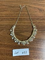 Full view of gold tone necklace with rhinestone accents on wooden surface with lot number.