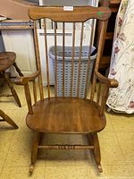 Front view of wooden Windsor style rocking chair showing spindle back, armrests, solid seat, and rockers.