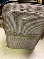 Close-up of the soft-sided suitcase exhibiting a brown and beige houndstooth pattern with front zipper pockets and telescoping handle.