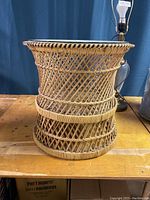 Full view of the wicker side table showing its cylindrical shape and weaving pattern on a wooden surface.