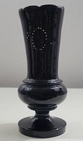 Full front view of the antique black amethyst glass vase with visible enamel painted oval pattern and scalloped rim.
