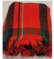 Folded red plaid wool blanket with visible fringed edges showing colors red, black, green