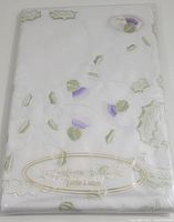 Original packaged folded tablecloth with visible embroidered green holly leaves and purple thistle flowers, white background.