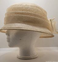 Side profile of the beige mesh hat showing shape and bow detail.