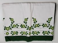 Photo of a white tea towel with green floral border and solid green hem edge, folded