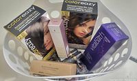 Photo showing packaged permanent cream hair color boxes, a large purple Vitabath moisturizing gel box, a pink SinfulColors nail polish bottle, a small perfume bottle, and multiple black and gold lipsticks arranged in a white basket.
