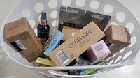 First photo shows a white laundry basket containing various boxed cosmetic products including multiple CoverGirl boxes and a black spray bottle.