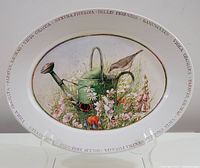 Full view of the oval serving platter showing the central watering can with bird and wildflower meadow design and text around rim.