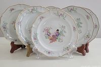 Set of six vintage Limoges porcelain plates arranged on stands showing decorative chinoiserie painted scenes with floral accents and gold edging.