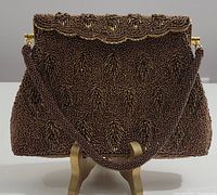 Front view of copper tone beaded evening bag on stand with strap visible