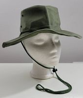 Front view of olive green ladies Tilley style hat on mannequin head showing wide brim and snap-up side button.