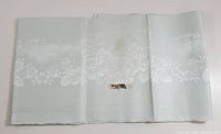 Full view of the pale green damask tablecloth showing the floral pattern and discoloration spot.