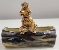 Close-up side view of the ceramic trinket dish in the shape of a wood log with a sculpted poodle sitting on top.
