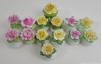 Top view of 14 vintage fine bone china salt and pepper shakers with colorful floral tops in pink, yellow, and purple shades, arranged in a triangular pattern.