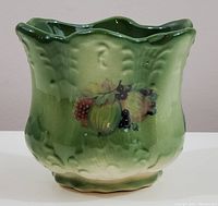 Front left angle view of green ceramic jardinere showing hand painted fruit design and scalloped top edge.