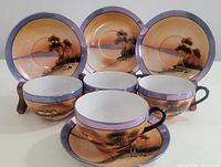 Four vintage Japanese hand painted lustreware cups and saucers with landscape design in the background with purple lustre borders.