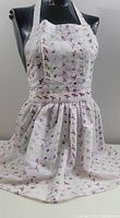 Front view of white eyelet fabric apron with purple floral pattern displayed on mannequin.
