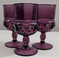 Front view of 3 amethyst purple goblets showing ornate embossed pattern, short stems, and wide bases.