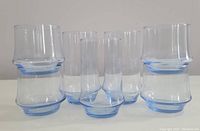 Seven powder blue tinted beverage glasses grouped together, showing different heights and shapes