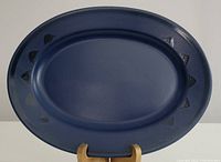 Full front view of the navy blue oval serving platter showing the smooth surface and triangular edge details.