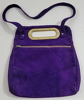 Full view of vintage purple suede handbag with carry strap and metal oval handle showing front side with zipper pocket.
