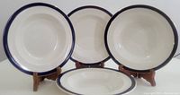 Four vintage Alfred Meakin soup bowls arranged side by side and one horizontally front-facing, showing blue rim detail and overall shape.
