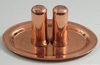 Front view of two copper salt and pepper shakers on an oval etched copper tray against a white background.