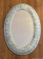 Full front view of the oval mirror showing the metal frame and beveled glass