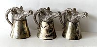 Three pewter shot glasses shaped like rams heads, shown front view with twisted horn handles